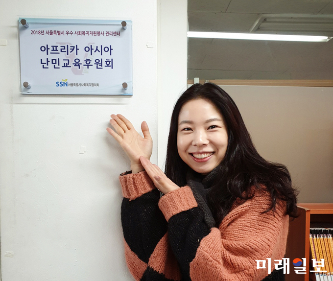 ADRF 최우정 팀장이 자원봉사 우수센터인증 현판을 가르키고 있다./사진=아프라카아시아난민교육후원회 제공