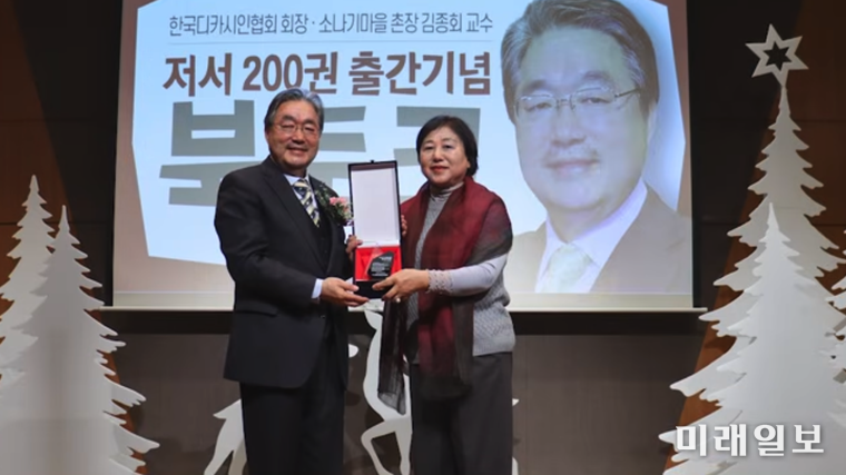 김종회 황순원문학촌 소나기마을 촌장(문학평론가)이 지난해 12월 26일, 황순원문학촌 소나기마을 수숫단강당에서 열린 '저서 200권 출간기념 북토크'에서 박수현 서울양천디카시인협회 회장으로부터 축하패를 전달 받고 있다./사진=황순원문학촌 소나기마을 문학강연 채널 '문학마실' 제공